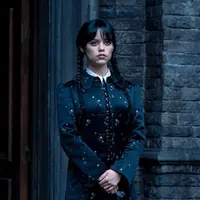 Jenna tampil formal dengan outer dress motif kembang berwarna hitam. Selain pakaian yang serba hitam, karakter yang ia mainkan juga memakai riasan wajah bagian mata yang mencolok dan cat kuku berwarna hitam. (Instagram/@diet_prada/@netflix)