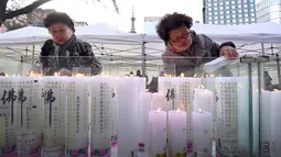 Dua orang wanita menyalakan lilin untuk mendoakan keberhasilan anak dan kerabatnya dalam mengikuti tes kemampuan Skolastik College tahunan di Seoul (23/11). Para ibu ini mengunjungi kuil Buddha Jogye untuk mendoakan anak mereka. (AFP Photo/Jung Yeon-Je)