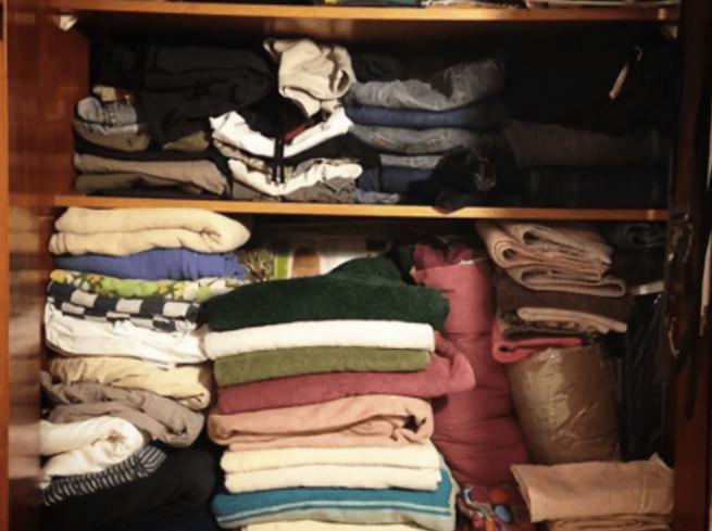 Kucing dalam tumpukan baju di lemari pakaian.