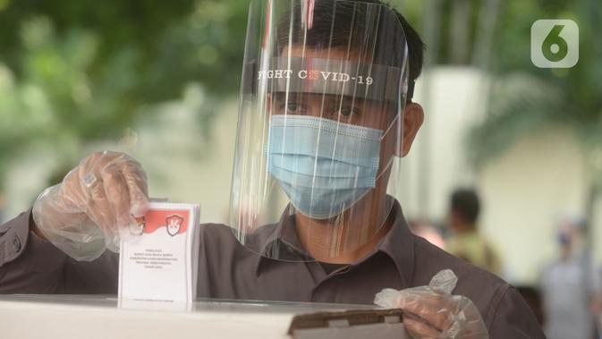 Petugas memakai face shield memasukan surat pemungutan suara dalam pemilihan serentak 2020 saat simulasi di Halam Kantor KPU, Jakarta, Rabu (22/7/2020). Simulasi pemungutan suara di TPS dengan menerapkan protokol kesehatan Covid-19. (merdeka.com/Imam Buhori)
