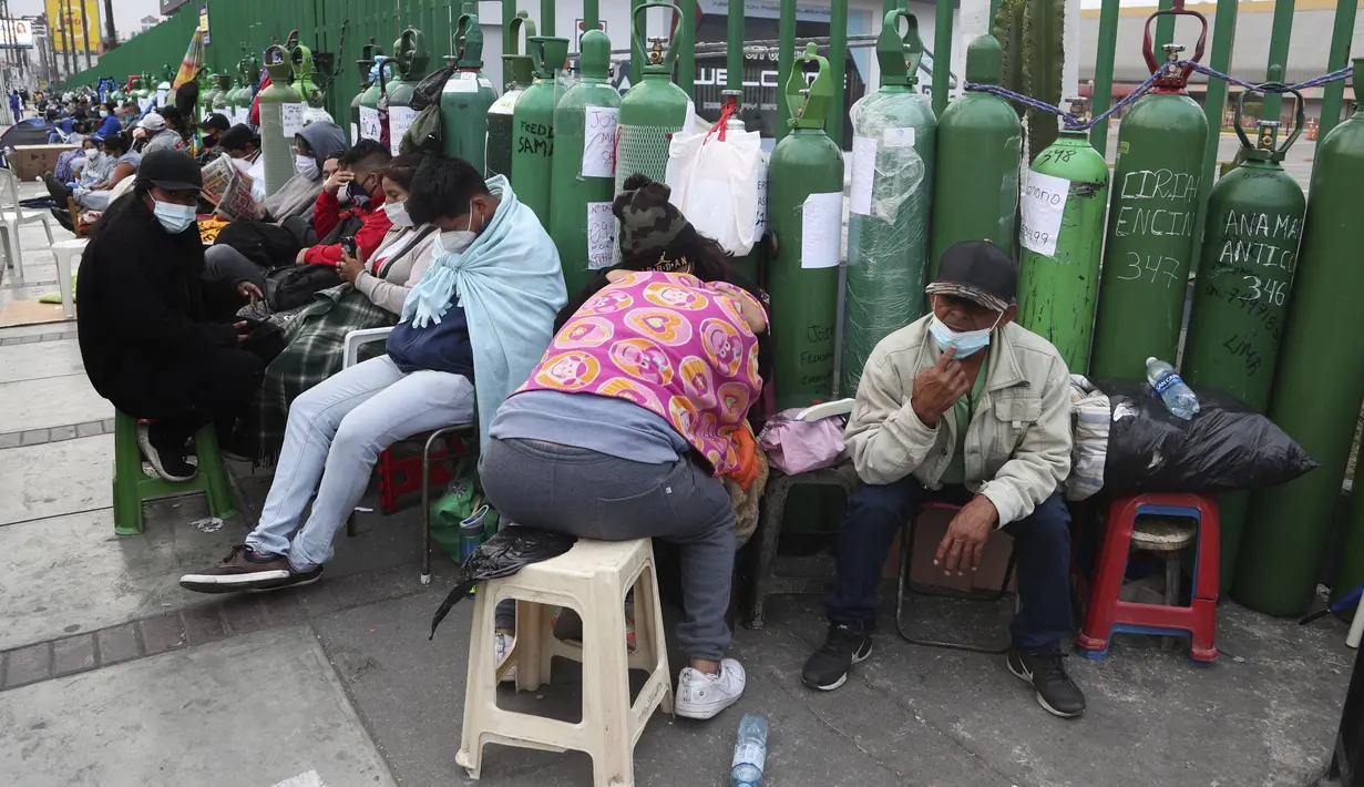 Orang-orang duduk di dekat tabung oksigen kosong mereka saat menunggu toko isi ulang dibuka di lingkungan San Juan de Lurigancho di Lima, Peru, Senin (22/2/2021). Mereka antre tabung oksigen untuk anggota keluarga yang membutuhkan di tengah gelombang kedua pandemi Covid-19. (AP Photo/Martin Mejia)