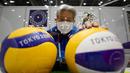 Seorang sukarelawan yang mengenakan masker sebagai tindakan pencegahan terhadap virus Covid-19 berpose dengan bola voli di belakang kaca pelindung di pusat media menjelang pembukaan Olimpiade Tokyo 2020 di Tokyo pada 20 Juli 2021. (AFP/Franck Fife)