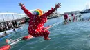 Seorang peserta dalam kostum Badut melompat ke dalam air pada kompetisi renang 'Copa Nadal' di Port Vell, Barcelona, Rabu (25/12/2019). Lebih dari 300 peserta menempuh jarak sejauh 200 meter pada tradisi lama yang digelar  saat hari Natal tersebut. (Josep LAGO / AFP)