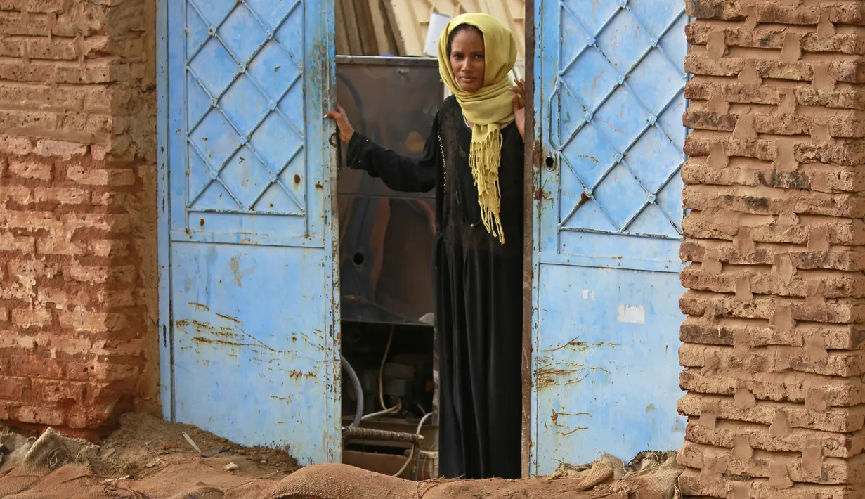 Seorang wanita Sudan berdiri di depan pintu rumahnya di area banjir alqamayir di kota kembar ibu kota Omdurman (26/8/2020). (AFP Photo/Ashraf Shazly)