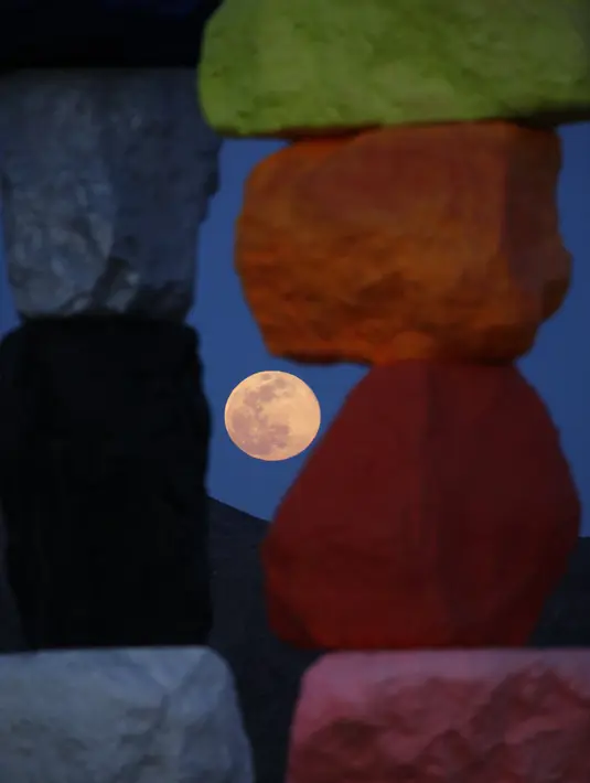 Supermoon terlihat dari celah instalasi seni Seven Magic Mountains karya seniman Ugo Rondinone di Las Vegas, Amerika Serikat, Selasa (7/4/2020). Warna-warni tumpukan batuan besar di tengah Gurun Nevada menjadikan Seven Magic Mountains terlihat sangat Instagramable. (AP Photo/John Locher)