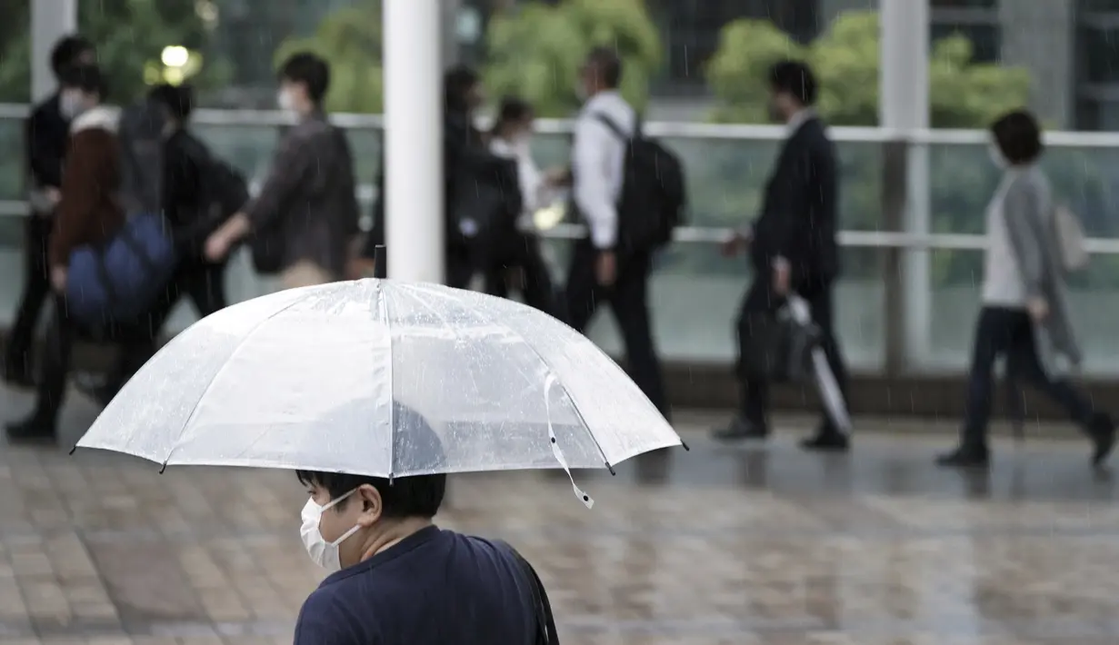 Seorang komuter yang mengenakan masker dan menggunakan payung berjalan jam sibuk di Stasiun Shinagawa, Tokyo, Jumat (1/10/2021). Pemerintah Jepang mencabut keadaan darurat di semua wilayah pada 1 Oktober 2021. (AP Photo/Eugene Hoshiko)