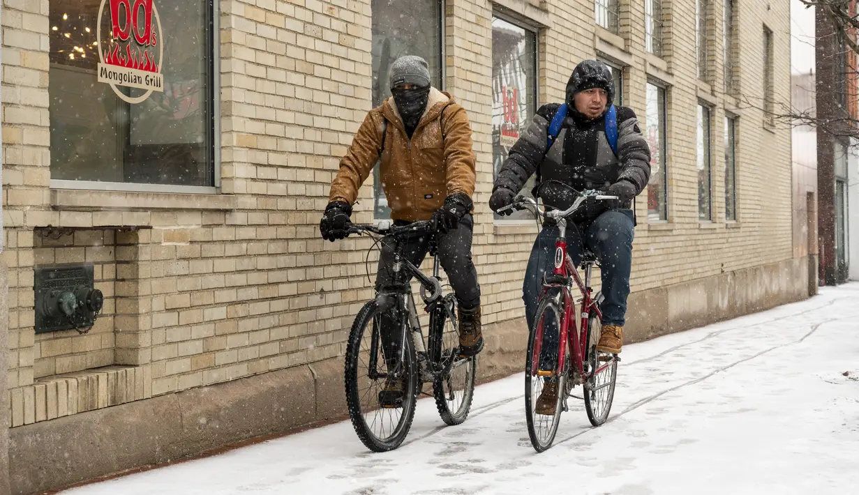 Dua pria bersepeda di Washington Street saat salju turun di Ann Arbor, Michigan, Rabu (2/2/2022). Badai musim dingin besar dengan jutaan orang Amerika di jalurnya membawa campuran hujan dan salju ke bagian tengah Amerika Serikat. (Jacob Hamilton/Ann Arbor News via AP)
