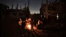 Warga Palestina duduk di sekitar api saat mereka bermalam di samping rumah mereka yang hancur di kota Beit Hanoun, Jalur Gaza utara, Rabu (26/5/2021). Serangan udara Israel selama 11 hari ke Jalur Gaza mengakibatkan ratusan jiwa tewas, ribuan rumah dan bangunan hancur. (AP Photo/Khalil Hamra)