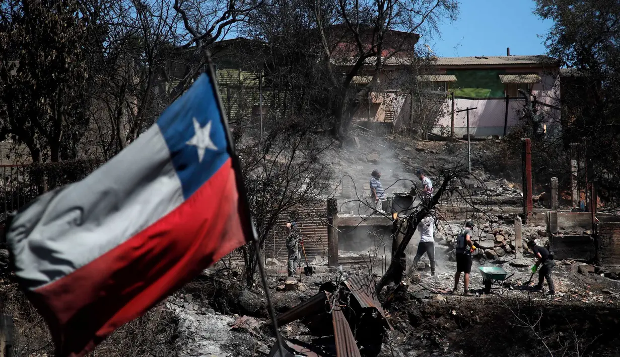 Bendera Chili berkibar ketika warga membersihkan lahan dan rumah mereka yang terbakar di Villa Independencia, wilayah Valparaiso, Chili pada tanggal 5 Februari 2024. (Javier TORRES/AFP)