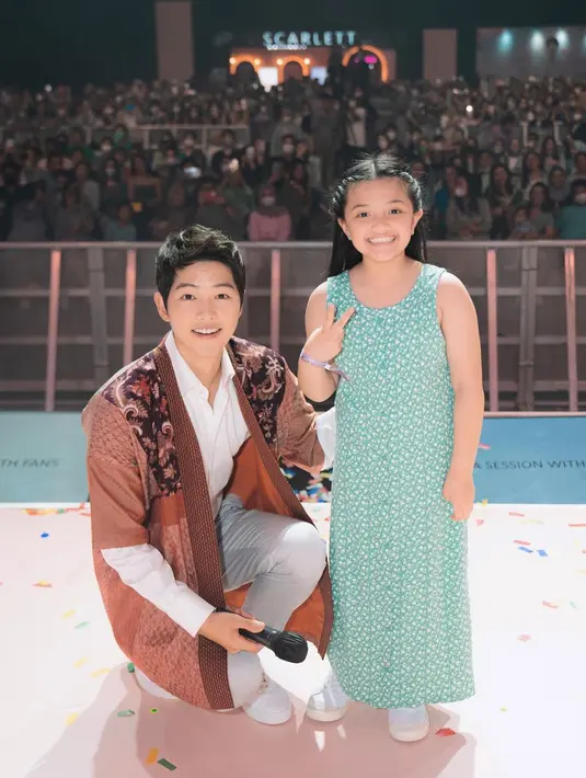 Ini mungkin jadi satu momen yang tak terlupakan, saat Arsy bisa berpose di atas panggung bersama Song Joong Ki. Arsy tampil cantik dengan dress tanpa lengan berwarna hijau, menunjukkan senyum lebarnya dan pose dua jari yang menggemaskan. Foto: Instagram.