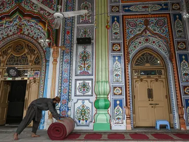Umat Muslim menggulung karpet sajadah dari aula utama masjid menyusul pembatasan baru pemerintah baru di Rawalpindi, Senin (5/4/2021). Pejabat kesehatan Pakistan telah meminta masjid-masjid mengambil langkah-langkah khusus untuk menahan penyebaran COVID-19 selama Ramadan. (Aamir QURESHI/AFP)