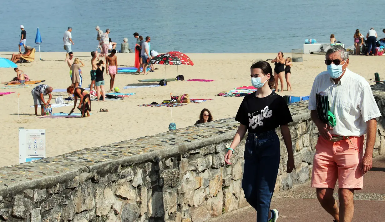 Orang-orang memakai masker berjalan di sepanjang pantai di Saint Jean de Luz, Prancis barat daya, Selasa (27/7/2021). Otoritas setempat di Prancis memberlakukan kembali mandat masker dan pembatasan COVID-19 lainnya karena penyebaran varian delta menyebabkan rawat inap meningkat lagi. (AP/Bob Edme)