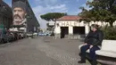 Seorang wanita duduk di taman yang berada dekat dengan mural Diego Armando Maradona di San Giovanni a Teduccio, Italia (28/2). Mural tersebut karya seniman asal Italia yang bernama Jorit Agoch. (AFP/Renato Esposito)