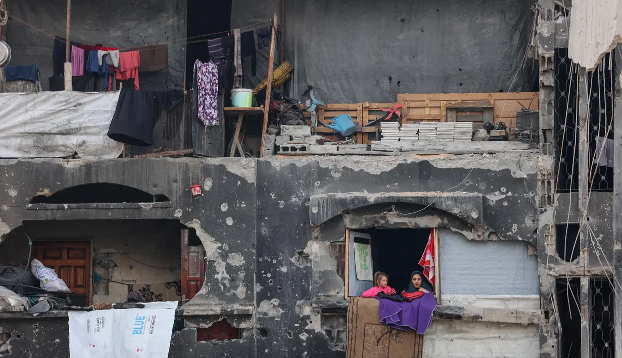 Anak-anak perempuan Palestina yang mengungsi melihat keluar rumah yang rusak tempat mereka berlindung di Beit Lahia di Jalur Gaza utara, menjelang waktu berbuka puasa selama bulan suci Ramadan pada 9 Maret 2025. (Omar AL-QATTAA/AFP)