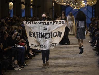 Seorang pengunjuk rasa memegang spanduk pada peragaan busana Louis Vuitton Spring/Summer 2022 di Paris, Selasa (5/10/2021). Pengunjuk rasa itu berjalan di atas catwalk Paris Fashion Week dengan membawa spanduk yang mengutuk dampak konsumsi berlebihan terhadap lingkungan (Vianney Le Caer/Invision/AP)