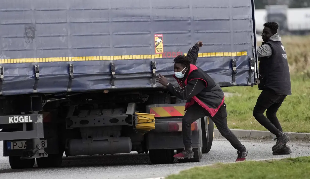 Para migran mencoba melompati truk untuk menyeberangi terowongan menuju Inggris di Calais, Prancis pada 14 Oktober 2021. Dalam praktik berbahaya dan berpotensi mematikan, ia mencoba melewati terowongan yang dijaga ketat yang menghubungkan kedua negara dengan bersembunyi di truk (AP/Christophe Ena)
