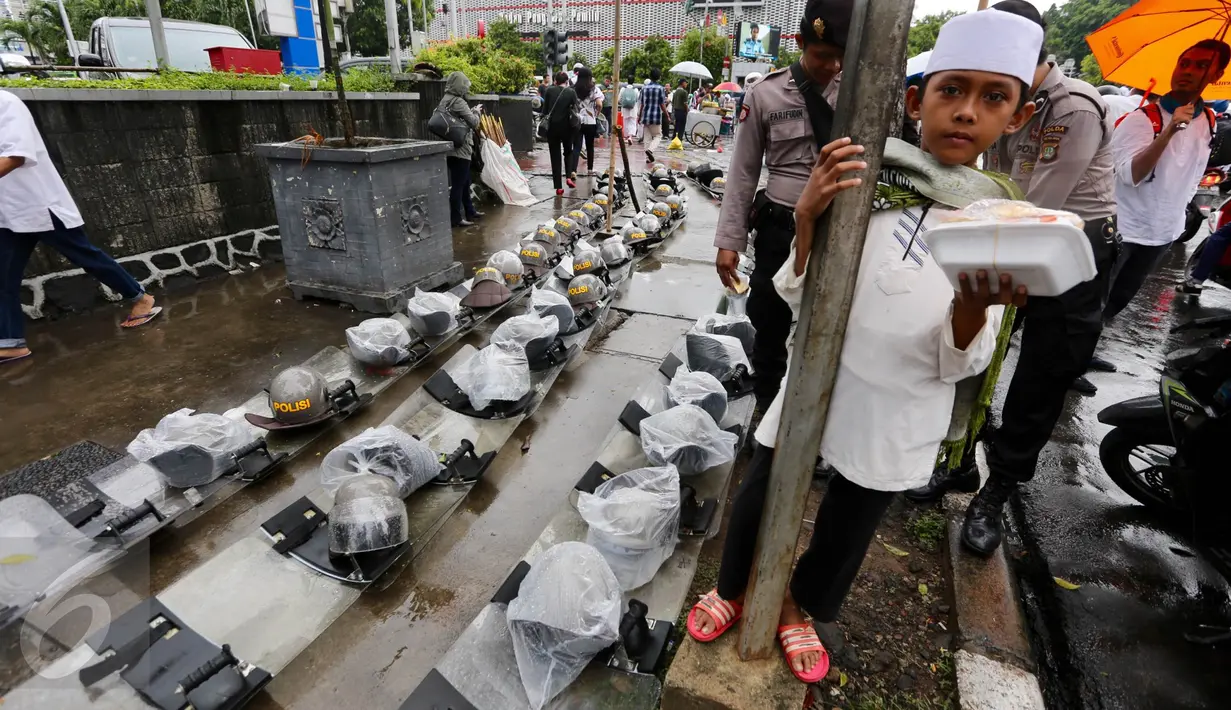 Seorang anak berpose di dekat helm dan tameng polisi yang diletakan di trotoar kawasan Sarinah, Jakarta, Jumat (2/12). Meski aksi 2 Desember telah usai, mereka tetap berjaga sampai situasi kondusif. (Liputan6.com/Ferbian Pradolo)