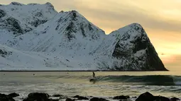 Peselancar menikmati gelombang ombak saat berselancar di pantai bersalju Flackstad di Kepulauan Lofoten, Lingkar Arktik, pada 12 Maret 2016. Suhu laut mencapai 5 derajat celcius dan suhu udara hingga 0 derajat celcius. (AFP/Olivier Morin)