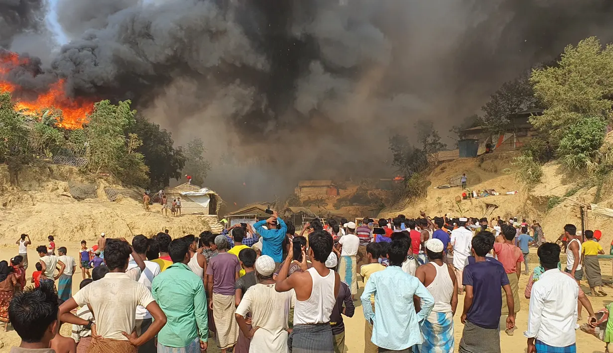 Pengungsi Rohingya menyaksikan asap membubung menyusul kebakaran di kamp pengungsi Rohingya di Balukhali, Bangladesh selatan (22/3/2021). Api menghancurkan ratusan tempat penampungan dan menyebabkan ribuan orang kehilangan tempat tinggal, kata pejabat dan saksi. (AP Photo/Shafiqur Rahman)