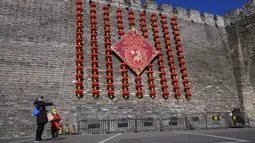 Seorang wanita dan anak  bermain dengan pesawat kertas di dekat dekorasi lentera untuk Tahun Baru Imlek jelang Tahun Baru Imlek di di sisa-sisa tembok kota di Beijing, Kamis (27/1/2022). (AP Photo/Andy Wong)