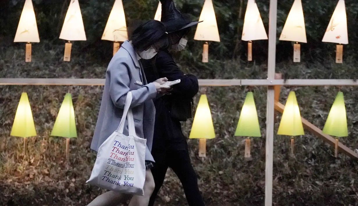 Pengunjung berjalan melewati lentera dan dekorasi bercahaya yang dinyalakan untuk menandai peringatan 100 tahun Kuil Meiji Jingu Shinto di Tokyo, Jumat (30/10/2020). Meiji Jingu, dibangun untuk memberi penghormatan kepada Kaisar Meiji dan Permaisuri Shoken pada tahun 1920 (AP Photo/Eugene Hoshiko)