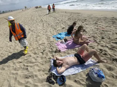 Seorang pekerja berjalan saat pengunjung pantai beristirahat di Huntington Beach, California, Senin (11/10/2021). Pantai Huntington membuka kembali garis pantainya setelah hasil pengujian air kembali dengan jumlah racun terkait minyak yang tidak terdeteksi di air laut. (AP Photo / Ringo HW Chiu)