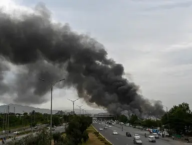 Pengendara melintas di sebuah jalan ketika asap membumbung dari kebakaran yang terjadi di sebuah pasar mingguan di Islamabad pada tanggal 10 Juli 2024. (Aamir Qureshi/AFP)