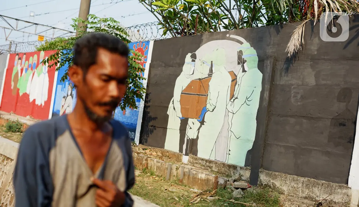Warga melintas di depan mural bertema covid-19 di Bukit Duri, Jakarta, Minggu (30/8/2020). Mural yang dibuat petugas PPSU bertujuan untuk mengingatkan masyarakat akan bahaya covid-19, sehubungan dengan masih tingginya jumlah kasus positif covid-19 di Jakarta. (Liputan6.com/Immanuel Antonius)