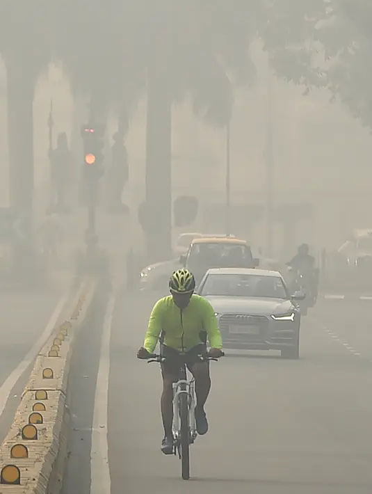 Seorang pengendara sepeda mengenakan masker menembus kabut asap pekat yang menyelimuti jalan di New Delhi, Selasa (12/11/2019). Kabut asap kembali menyelimuti ibu kota India setelah akhir pekan dengan udara cerah dan cuaca yang lebih baik. (Photo by Money SHARMA / AFP)