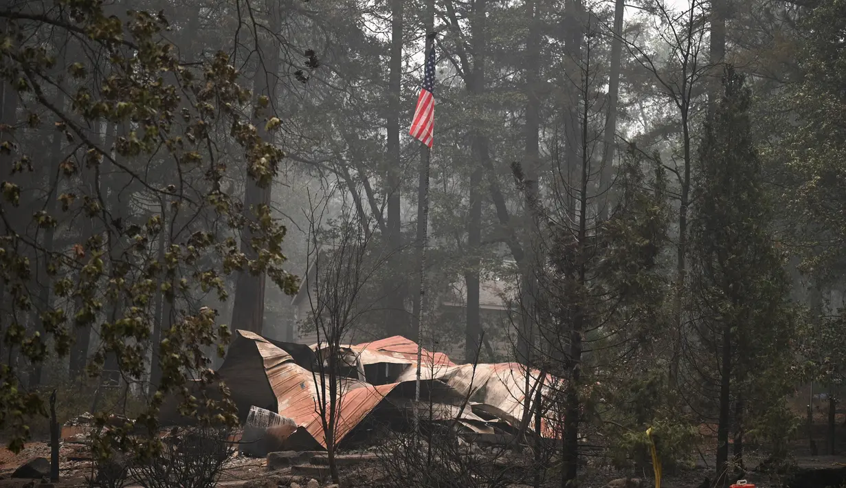 Sebuah bendera Amerika terlihat di atas properti yang terbakar dalam Kebakaran Dixie Fire di daerah Air Terjun India di Plumas County, California (26/7/2021). Api menghanguskan beberapa tempat tinggal di daerah tersebut. (AFP/Robyn Beck)