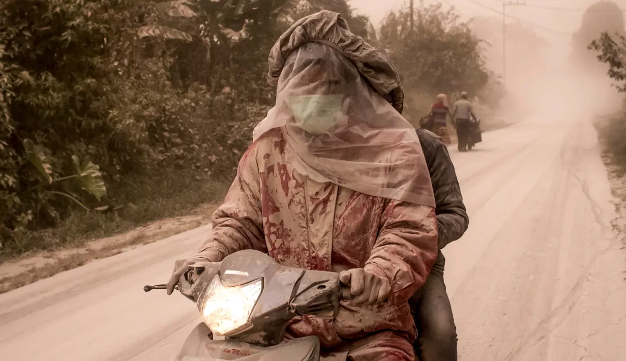 Pengendara motor menutupi wajahnya dari abu vulkanik akibat erupsi Gunung Sinabung di Desa Tiga Pancur, Karo, Sumatera Utara, Rabu (2/8). Lontaran abu Gunung Sinabung mencapai ketinggian 4,2 km dan luncuran awan panas sejauh 4,5 km. (IVAN DAMANIK/AFP)