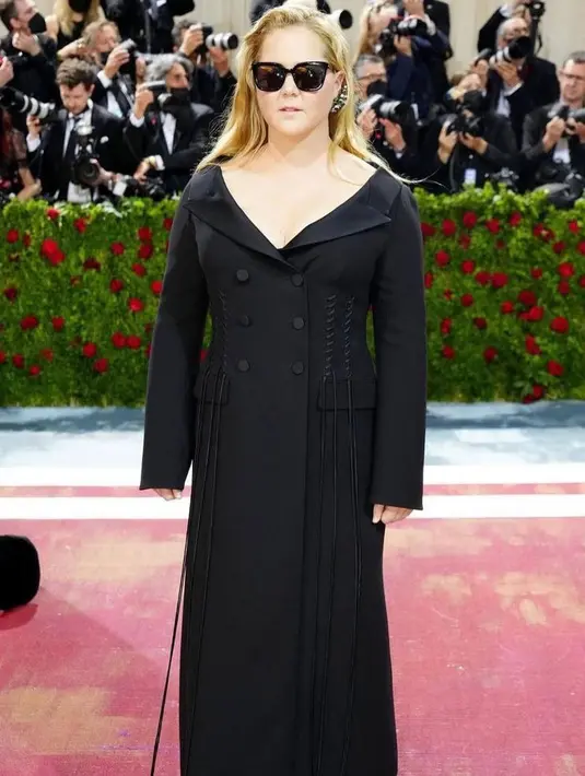 <p>Amy Schumer, tampak muram di karpet dengan gaun serba hitam, dengan tali panjang yang menggantung di atasnya. Dia juga memakai kacamata hitam. (Instagram/speakingvogue).</p>