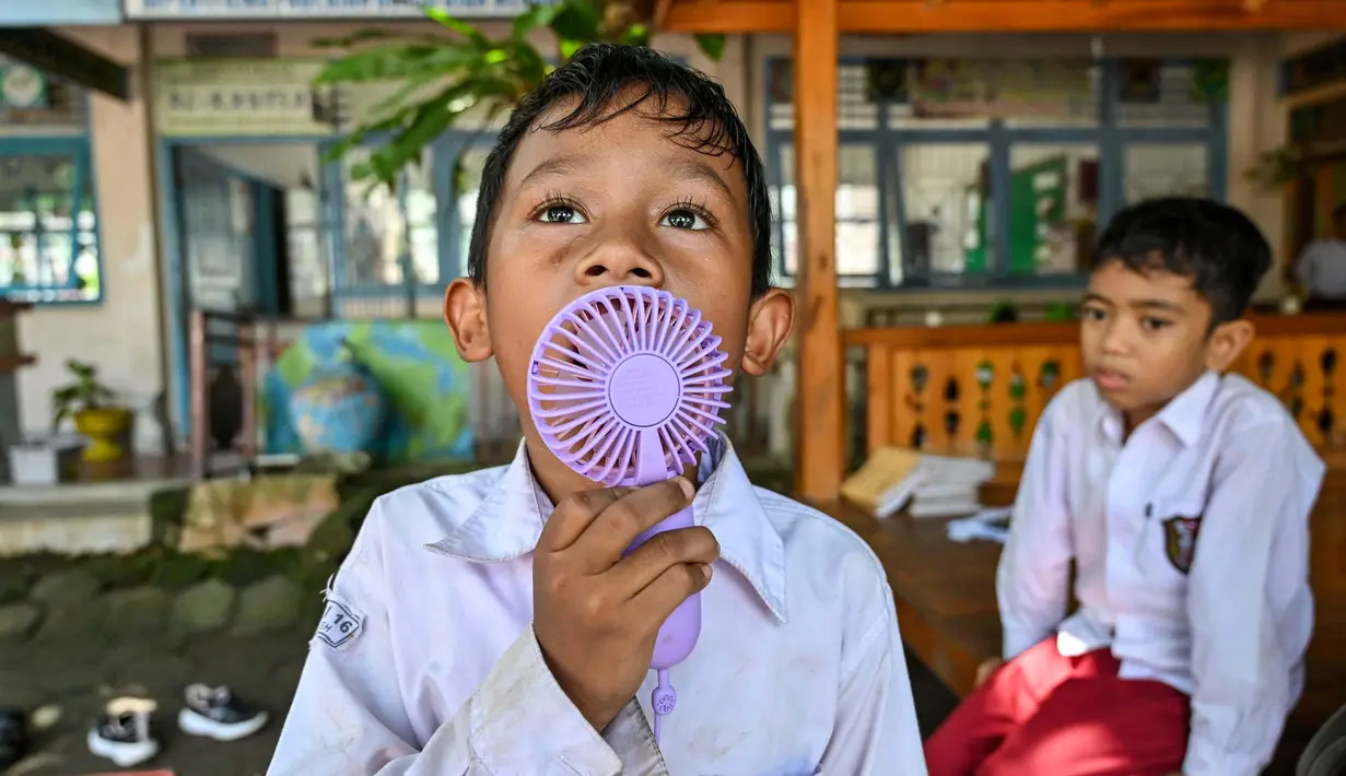 Seorang siswa menggunakan kipas angin portabel saat belajar di luar kelas selama gelombang panas di sebuah sekolah dasar di Banda Aceh pada 7 Mei 2024. (CHAIDEER MAHYUDDIN/AFP)