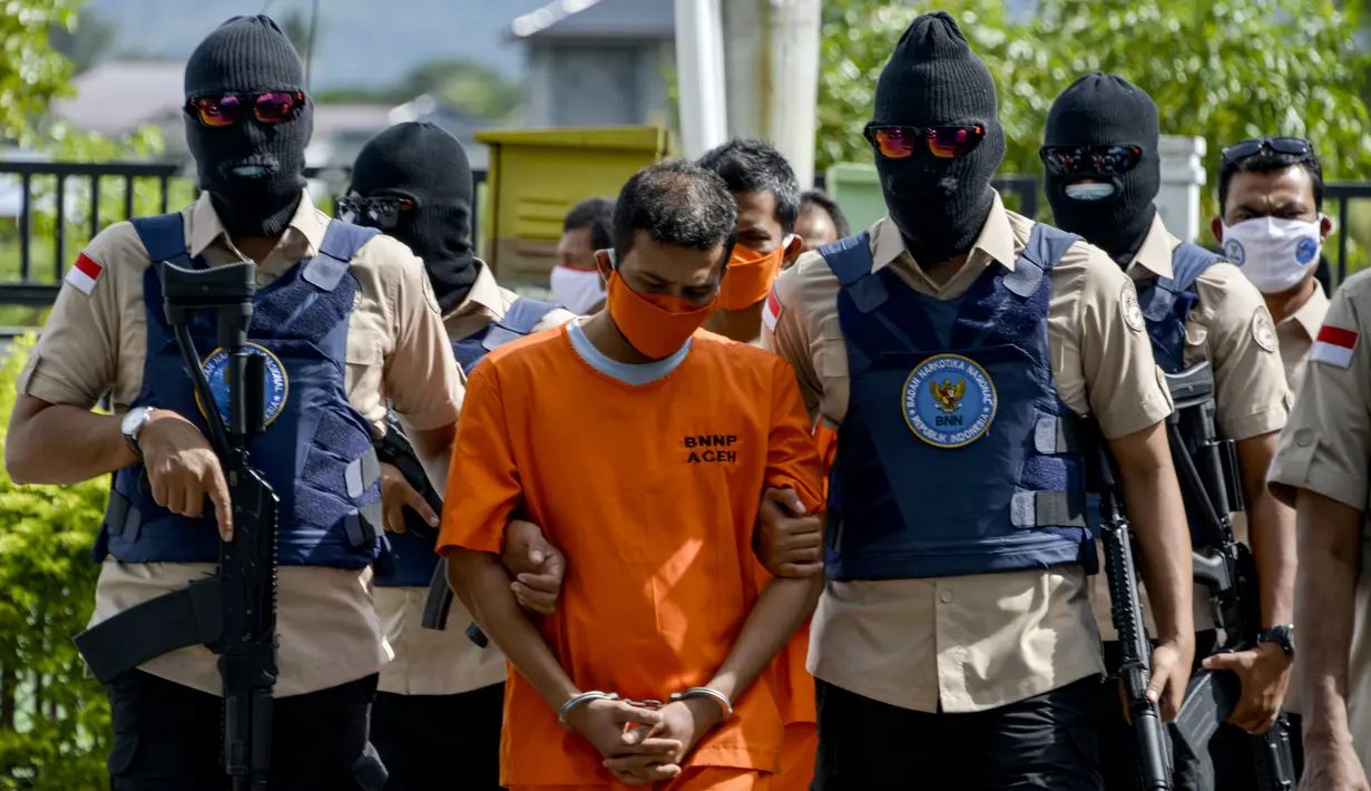 Petugas Badan Narkotika Nasional Indonesia (BNN) mengawal dua pria lokal yang diduga menyelundupkan sabu pada konferensi pers di Banda Aceh (13/10/2020). (AFP Photo/Chaideer Mahyuddin)