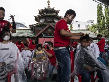 Penata rambut melakukan cukur rambut gratis saat acara amal di Surabaya, Jawa Timur, Senin (8/11/2021). Layanan cukur rambut gratis ini dilakukan kepada 100 anak yatim piatu. (Juni Kriswanto/AFP)