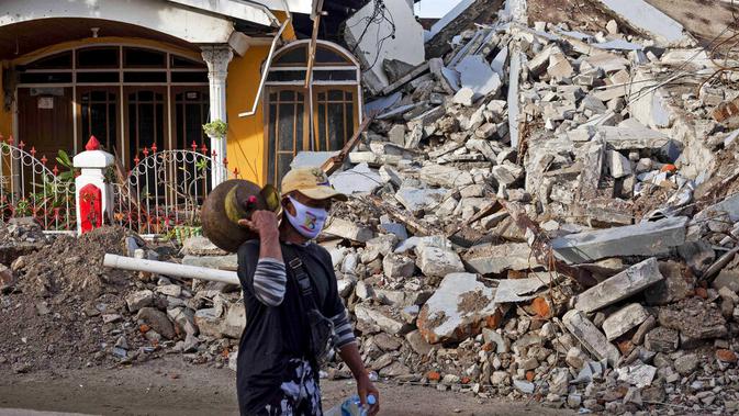 Seorang pria berjalan melewati rumah yang ambruk akibat gempa di Mamuju, Sulawesi Barat, Indonesia, Senin (18/1/2021). BNPB menyatakan pelabuhan hingga rumah sakit di Kabupaten Mamuju rusak berat akibat guncangan gempa dengan magnitudo 6,2. (AP Photo/Yusuf Wahil)
