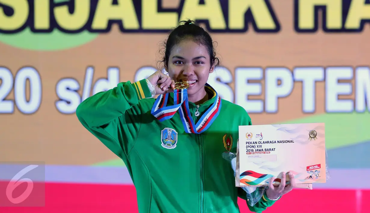 Lifter Jatim, Acchedya Jagaddhita menggigit medali emas usai berlomba di kelas 58kg PON XIX Jabar di Gymnasium Si Jalak Harupat, Kab Bandung, Rabu (21/9). Acchedya meraih emas dengan total angkatan 201kg. (Liputan6.com/Helmi Fithriansyah)