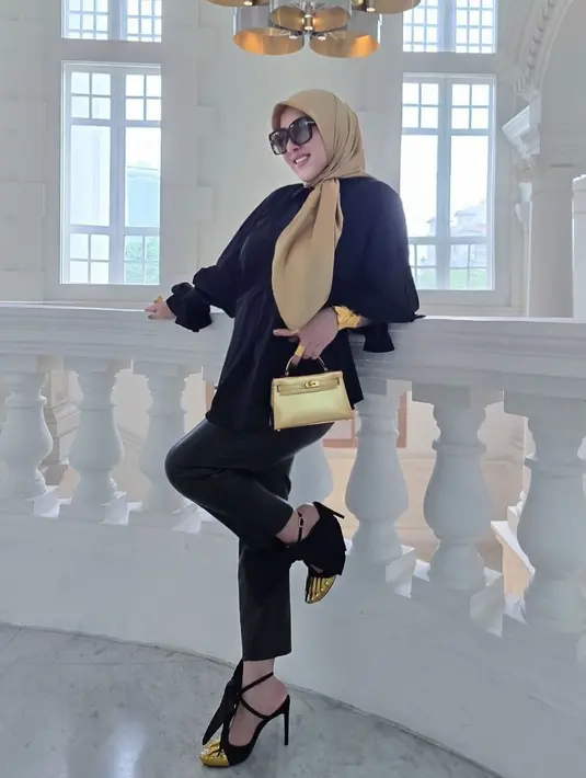 Syahrini mengenakan blouse hitam longgar yang dipadukan dengan celana kulit hitam slim-fit, memberikan kesan santai namun tetap berkelas.  [@princessyahrini].