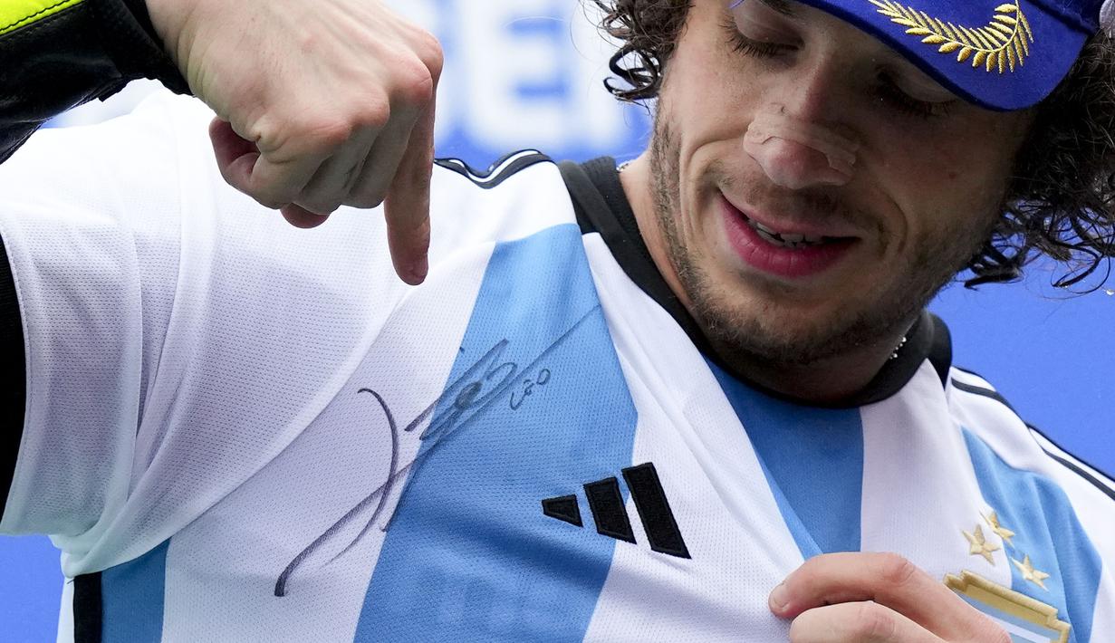 Pebalap Tim Mooney VR46, Marco Bezzecchi menunjukkan jersey Timnas Argentina bertandatangan Lionel Messi saat menjuarai MotoGP Argentina 2023 di Autódromo Termas de Río Hondo, Argentina, Senin (03/04/2023) dini hari WIB. Selebrasi tersebut diketahui meniru sang gurunya, Valentino Rossi yang dilakukan pada musim 2015 silam. (AP Photo/Natacha Pisarenko)