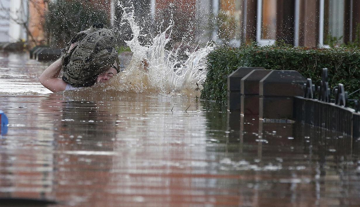 Warga tersandung saat melintasi banjir yang merendam jalan pemukiman di Carlisle, Inggris, Minggu (6/12). Puluhan ribu rumah tidak punya listrik karena Badai Desmond yang menyebabkan banjir di Inggris utara dan sebagian Skotlandia. (REUTERS/Phil Noble)