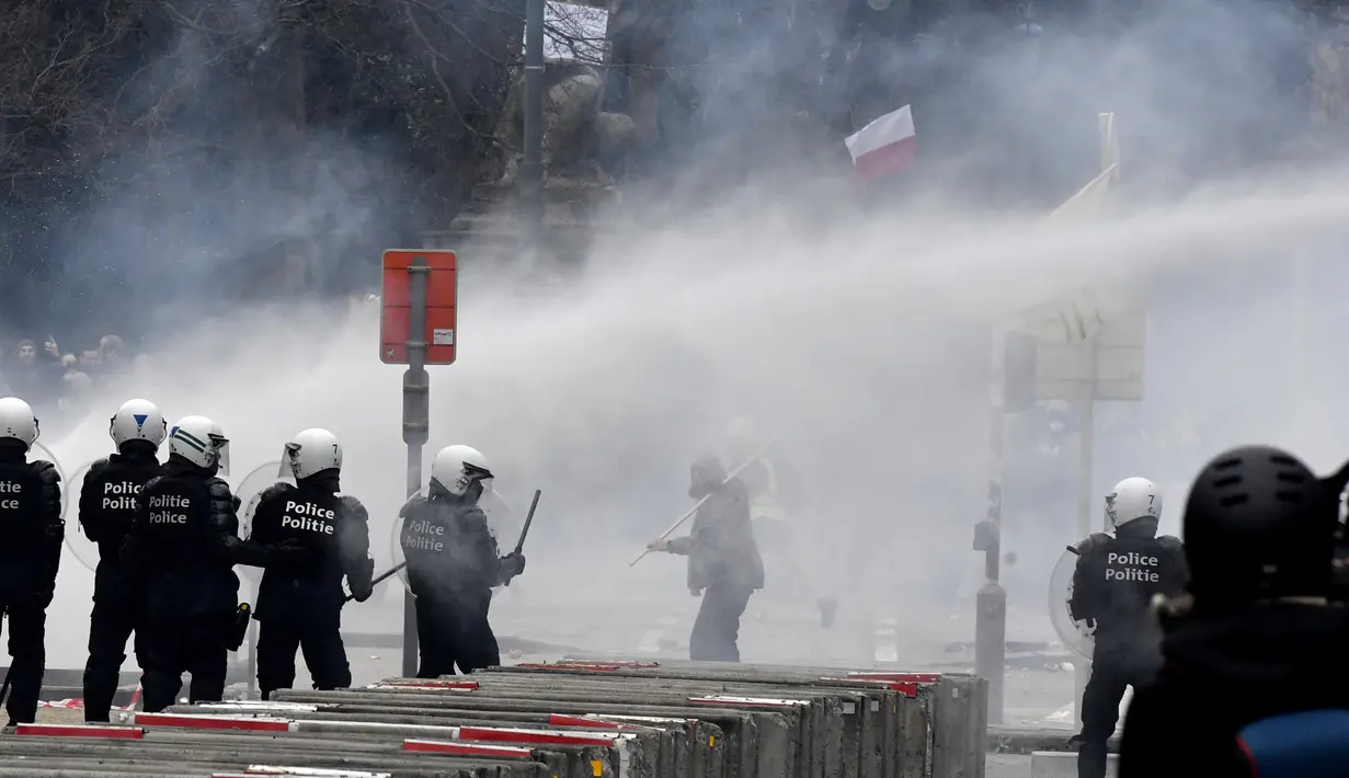 Polisi menembakkan water cannon ke arah pengunjuk rasa saat demonstrasi menentang tindakan Covid-19 di Brussel, Minggu (23/1/2022). Pengunjuk rasa berkumpul di ibu kota Belgia mengkritik dan menolak aturan pembatasan akibat COVID-19, salah satunya terkait vaksinasi. (AP Photo/Geert Vanden Wijngaert)