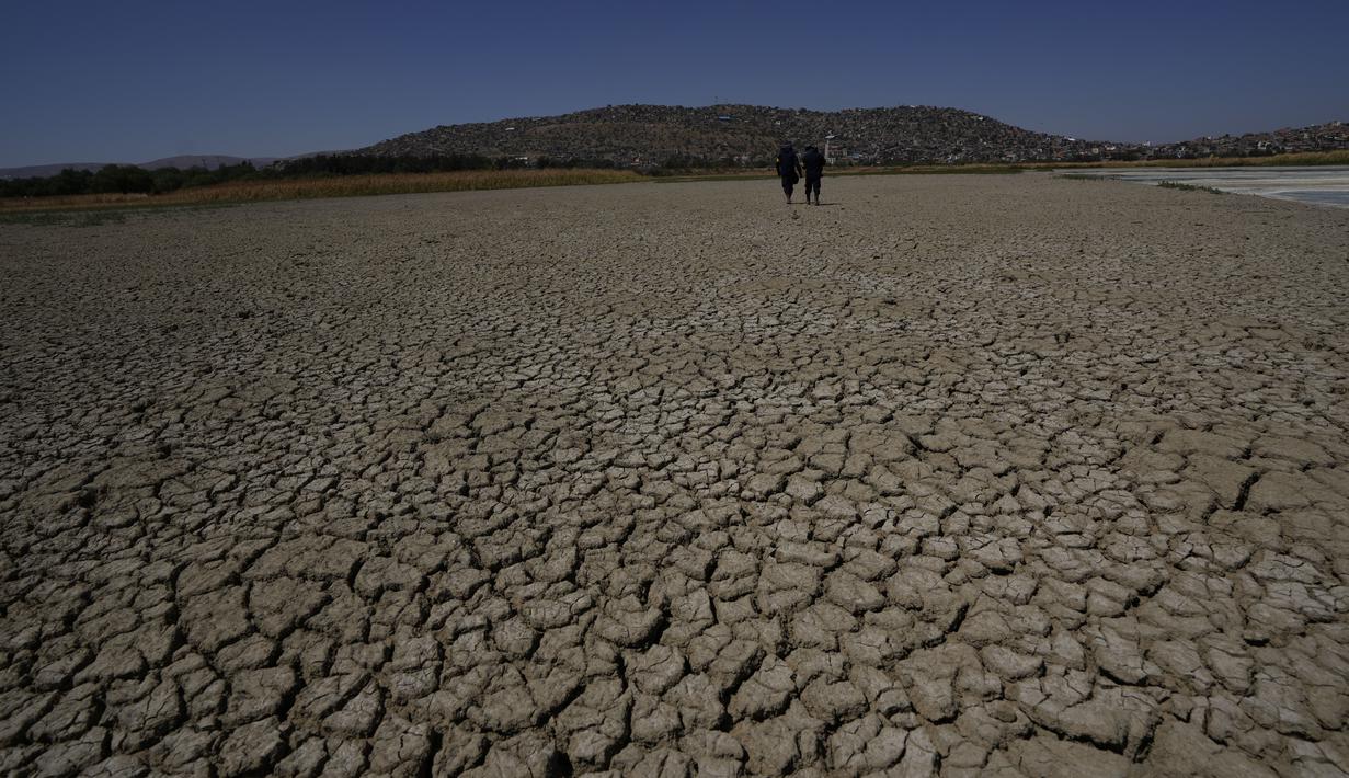 Penjaga kota berjalan di dasar laguna Alalay yang kering dan retak di Cochabamba, Bolivia, Jumat (18/11/2022). Dua laguna, Coña Coña dan Alalay, berada pada level kritis karena kurangnya hujan, penumpukan bahan organik dan penguapan di tengah peningkatan suhu. (AP Photo/Juan Karita)