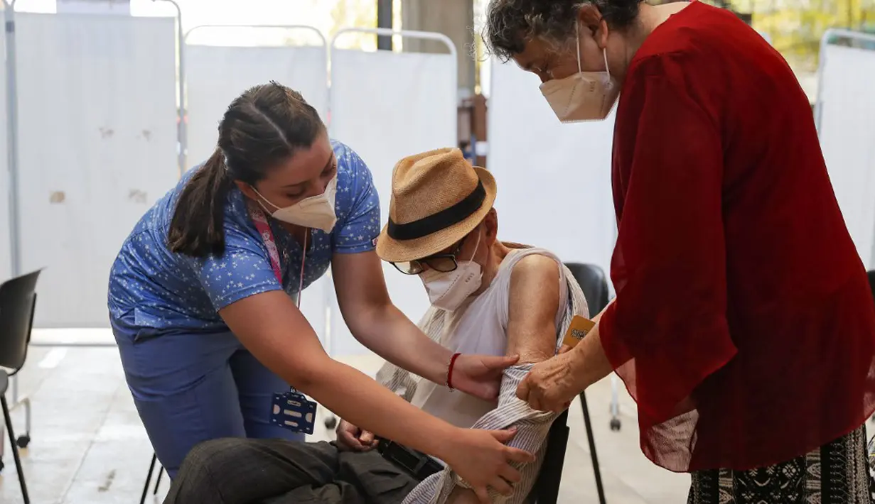 Seorang pria lansia didampingi istrinya (kanan) bersiap menerima suntikan BioNtech Pfizer COVID-19 sebagai booster di Santiago, Chile, 7 Februari 2022. Di tengah gelombang COVID-19, Chile memulai vaksinasi dosis keempat untuk warga di atas usia 55 tahun. (JAVIER TORRES/AFP)