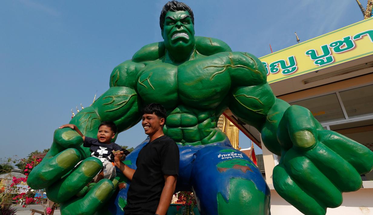 Seorang pria dan cucunya berpose dengan patung tokoh komik "Hulk" di kuil Tamru di provinsi Samut Prakan, Thailand, (3/3). Pihak Candi mengatakan telah menyiapkan patung-patung karakter komik Marvel untuk menarik pengunjung. (REUTERS/Chaiwat Subprasom)
