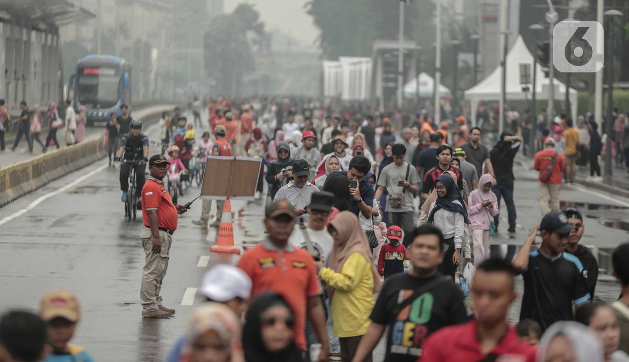 Petugas keamanan berjaga saat warga beraktivitas di car free day (CFD) kawasan Bundaran HI, Jakarta, Minggu (29/12/2019). Kendati tidak seramai saat cerah, warga yang berlari, jalan santai, atau swafoto masih menjadi pemandangan di area CFD usai hujan mengguyur Jakarta. (Liputan6.com/Faizal Fanani)