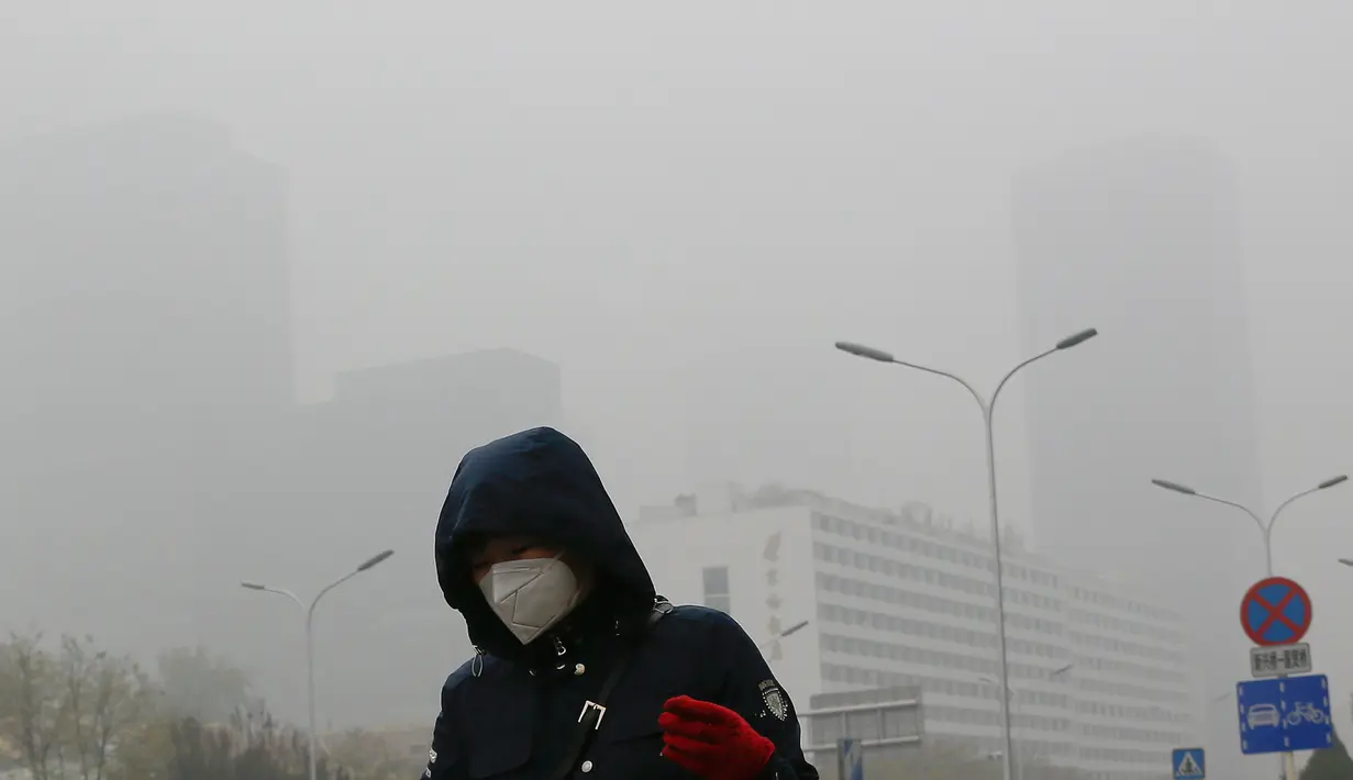 Seorang wanita beraktivitas mengenakan masker di sebuah jalan yang diselimuti kabut asap tebal di Beijing, China (14/11). Pihak berwenang mengeluarkan peringatan kuning untuk polusi udara buruk pada hari Rabu. (AP Photo/Andy Wong)