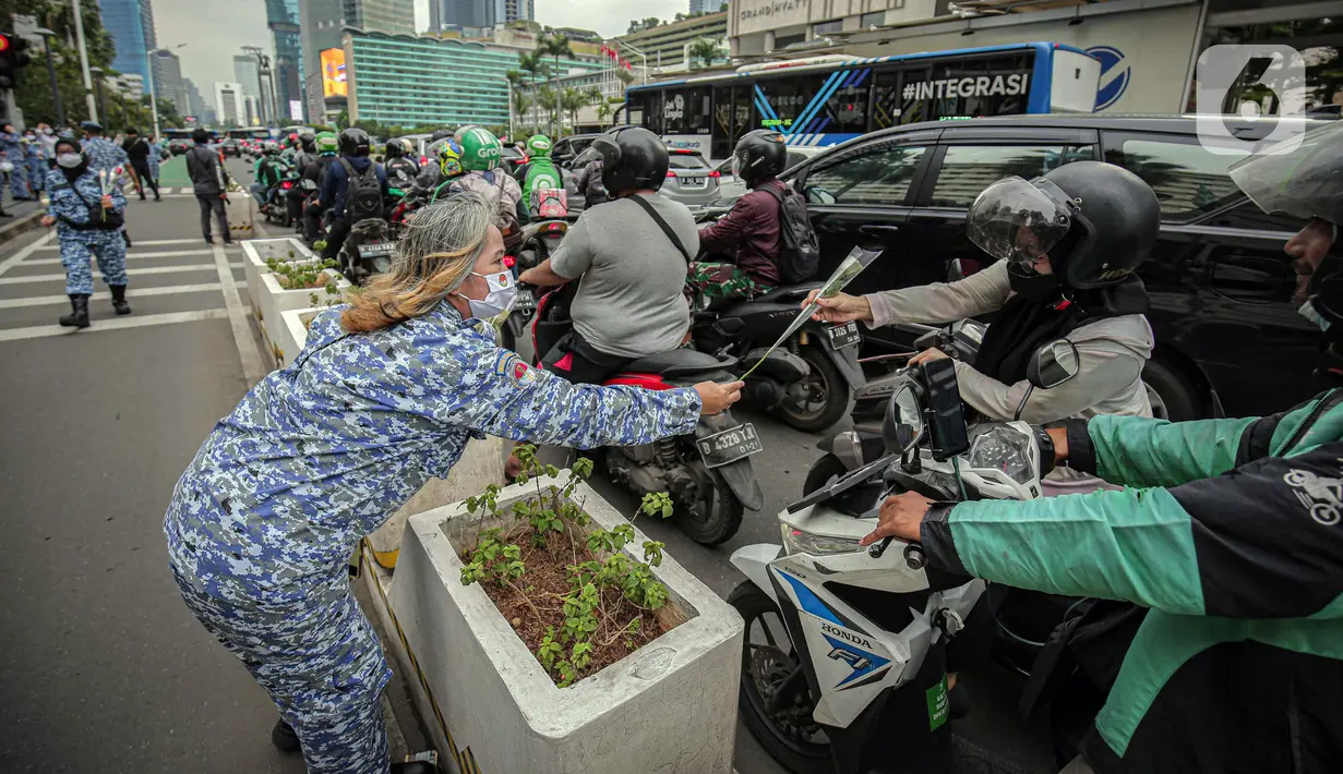 Perserta yang tergabung dalam Forum Kader Bela Negara DKI Jakarta membagikan bunga dan masker kepada pengguna jalan di Jalan Thamrin, Jakarta, Rabu (22/12/2021). Aksi tersebut merupakan bentuk apresiasi terhadap kaum perempuan terutama pada peringatan Hari Ibu. (Liputan6.com/Faizal Fanani)