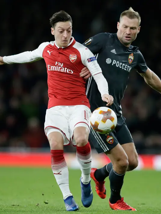 Pemain CSKA Moscow Aleksei Berezutski berebut bola dengan pemain Arsenal Mesut Ozil saat pertandingan Liga Eropa di stadion Emirates, London (5/4). Arsenal menang telak 4-1 atas klub Rusia, CSKA Moskow. (AP Photo / Tim Ireland)