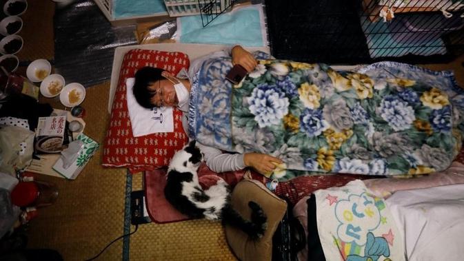 Sakae Kato berbaring di tempat tidur di sebelah Charm, seekor kucing yang ia selamatkan lima tahun lalu yang terinfeksi virus leukemia (Foto: Reuters).
