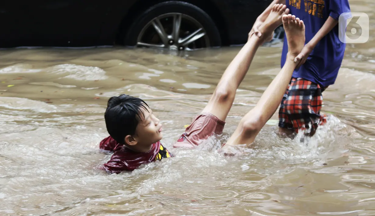 Anak anak bermain air di sebagian Jalan Bungur Besar Raya yang tergenang, Jakarta, Selasa (18/1/2022). Genangan air di sebagian Jalan Bungur Besar Raya dimanfaatkan anak-anak untuk bermain meski berbahaya. (Liputan6.com/Helmi Fithriansyah)